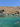 A scenic coastal cove on Gozo with clear turquoise water, rocky cliffs, several small boats anchored in the bay, and a few swimmers and snorkelers in the sea under a blue sky.